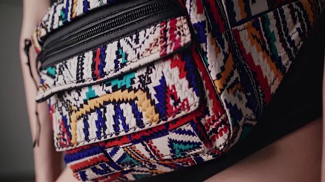A woman showcases a colorful waist pack, highlighting the waist pack's intricate design. The waist pack rests on the woman's hip as the waist pack stands out vividly.