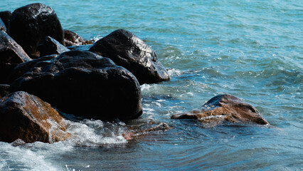 Close-up of clear blue water washing over dark, rugged coastal rocks