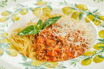 Delicious closeup of spaghetti bolognese topped with parmesan cheese and basil leaves on a decorated plate.