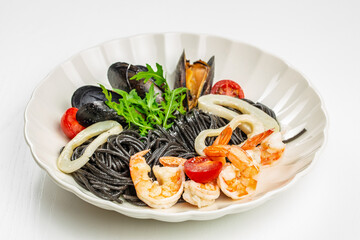 Delicious black squid ink pasta with shrimp, squid rings, mussels, arugula and cherry tomatoes served on a white plate. Gourmet seafood Italian cuisine