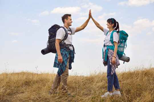 Hikers couple celebrate outdoors teamwork on trail. On a dry meadow, they high-five with backpack confidence, enjoying trekking and travel. Concept: success, partnership, outdoor adventure. - Powered by Adobe