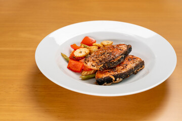 Grilled or Fried salmon steaks with fresh vegetables on plate on wooden table.