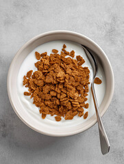 a top shot of a bowl of bran flakes, medium brown color of flakes on top of yogurt in a bowl