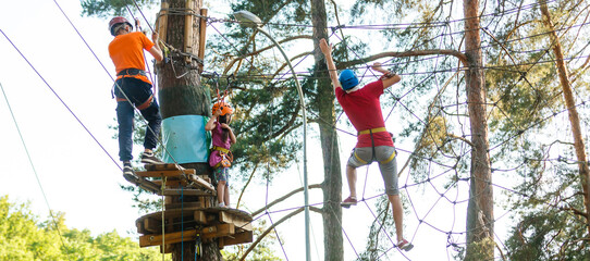 Adorable little girl enjoying her time in a rope playground structure at adventure park, her father supporting her, family weekend activities.