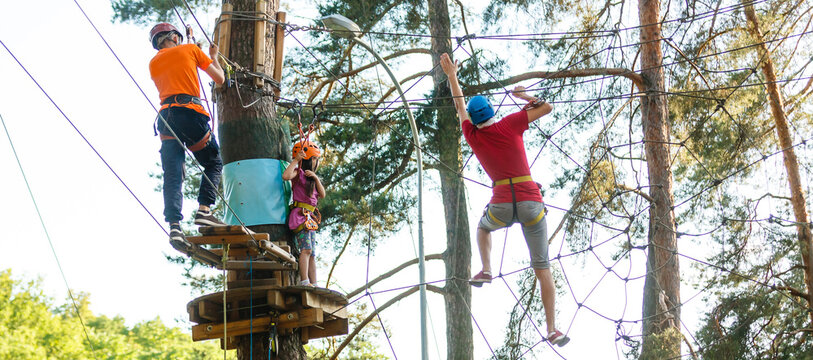 Adorable little girl enjoying her time in a rope playground structure at adventure park, her father supporting her, family weekend activities.