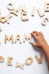 Child hand arranging wooden alphabet letters on white surface
