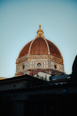 Fototapeta premium The magnificent terracotta-tiled dome of Cattedrale di Santa Maria del Fiore rises majestically above Florence rooftops against a serene blue sky. Iconic Renaissance architecture.