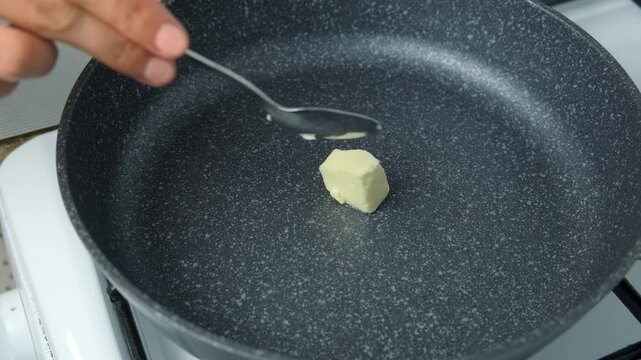 Woman cooking melting butter on frying pan mixing with metal spoon. Heating butter cubes preparing dish. Cuisine culinary prepare cook dish domestic food recipe ingredients. Healthy nutrition.