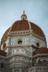 Fototapeta premium A stunning low-angle view of the iconic terracotta-tiled dome and intricate marble facade of Florence Cathedral (Duomo), a masterpiece of Renaissance architecture.