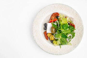 Top view of Greek salad with feta cheese, black and green olives, caper berry, sun-dried tomatoes, onion rings and lettuce leaves served on a white plate. Healthy Mediterranean food. copy space
