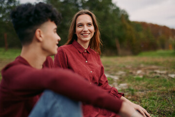 Obraz premium An authentic candid moment shows a smiling woman in a red shirt seated in a grassy field, radiating genuine connection and credibility through a simple, natural pose.