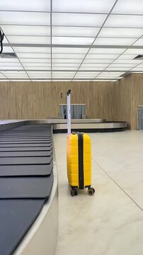 Yellow luggage near baggage carousel in airport arrived hall for baggage claim and traveling insurance business concept. Empty conveyor belt. Checked baggage, travel by aircraft. Vertical footage