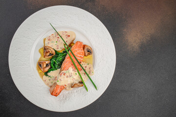 Top view of grilled salmon steak served with creamy sauce, sauteed spinach and mushrooms. Elegant gourmet seafood dish perfect for restaurant menu, healthy eating, or fine dining concept