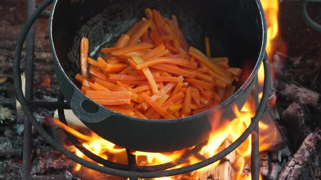 Carrots cooking fire, sliced carrots boiling in cast iron pot over open flame, outdoor traditional cooking