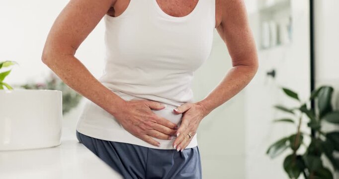 Hands, mature woman and stomach ache in home, menopause and health problem in bathroom. Constipation, discomfort and person with pain, abdomen cramps and sick with diarrhea in morning in house