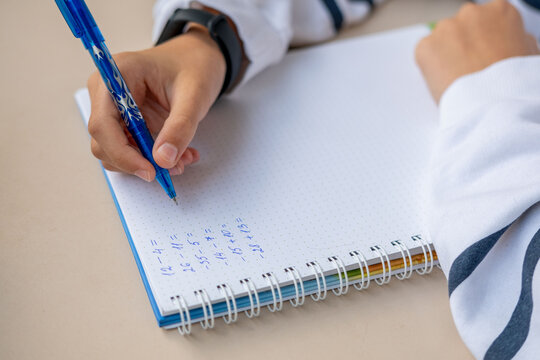 Hand writing math equations in dotted notebook with blue pen, solving arithmetic problems including negative numbers, educational activity, student homework, learning study session, school concept - Powered by Adobe