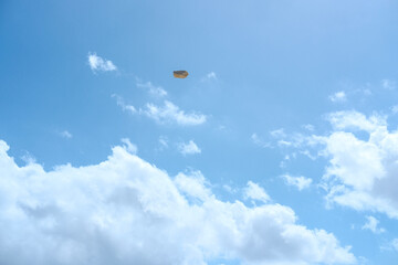 Small brown rock suspended against a bright blue sky with scattered white clouds, minimal composition with ample copy space.