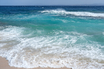 Turquoise surf washing onto a sandy shore; foamy white waves and clear water, close-up seascape texture.