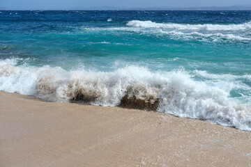 Powerful shore break with foamy crest hitting the beach; turquoise ocean beyond, energetic coastal...