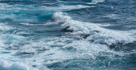Turquoise ocean waves roll toward a sandy beach, creating foamy surf along the shoreline.