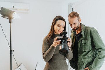 A man and a woman reviewing images on a camera in a bright studio setting. The scene conveys collaboration and creativity, showcasing teamwork and the artistic process in a professional environment.