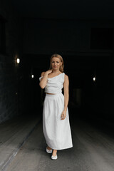 Blonde Caucasian woman with bob haircut in white dress on dark urban background