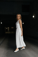 Blonde Caucasian woman with bob haircut in white dress on dark urban background
