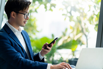 creative agency smart glasses asian male formal cloth conversation with smartphone freelance working with laptop at coworking area office space with freshness with blur office background