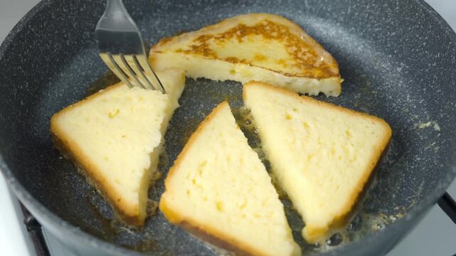 Close-up frying turning bread in egg on frying pan cooking toasts on kitchen at home. Cooking tasty homemade domestic meal food dish, hands close-up. Ingredient recipe cuisine culinary.