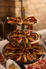 Elegant three-tiered serving stand filled with assorted bruschetta topped with cream cheese, roasted peppers, anchovies, and herbs, arranged for a buffet or catered event