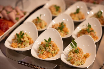 Elegant individual servings of salmon tartare with avocado and garnish, presented in white ceramic spoons on a reflective tray for a fine dining appetiser