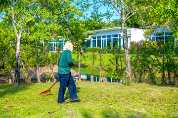 A janitor cleans the lawn area from leaves and mown grass. Hotel cleaning service.