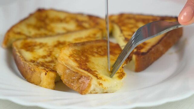 Cutting served fried toasts bread slices on plate to eat on kitchen at home, close-up view. Cooking tasty homemade domestic meal food dish, hands close-up. Ingredient recipe cuisine culinary.