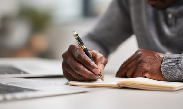 Focused african american man writing note in notebook at desk. Close up on hand