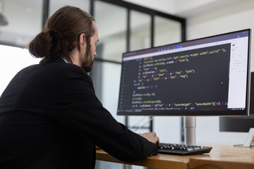 Software developer focused on writing and debugging code on desktop computer in modern office, representing programming, coding, software development, backend engineering, and tech industry work.