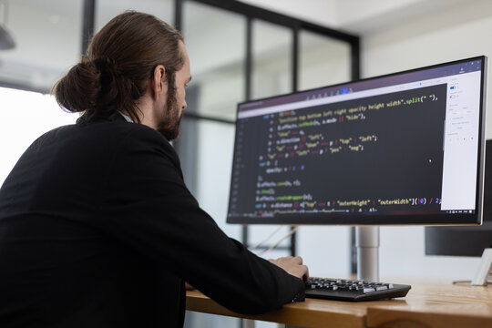Software developer focused on writing and debugging code on desktop computer in modern office, representing programming, coding, software development, backend engineering, and tech industry work.