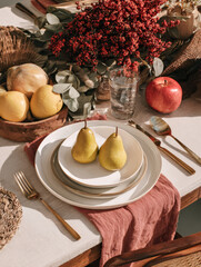 Autumn table setting with pears and pumpkins on a linen tablecloth. Warm and cozy atmosphere, perfect for seasonal food, rustic lifestyle, and festive decoration concepts.