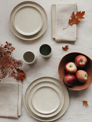 Top view of autumn table setting with plates, a bowl of apples, and colorful fall leaves. Cozy seasonal atmosphere, perfect for lifestyle, food photography, and festive decoration concepts