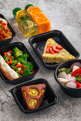 Flat lay of healthy meal prep containers with grilled chicken, vegetables, salad, frittata and fresh juice bottles