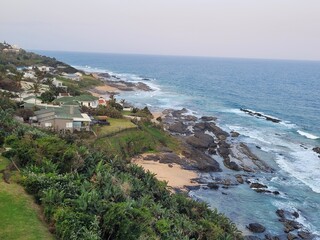 Sheffield Beach, KwaZulu-Natal, with ocean waves, rocky shore, and seaside homes on the South African coastline.