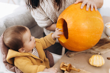 Family carving halloween pumpkin. Happy mother and cute baby son cutting pumpkin on table with...