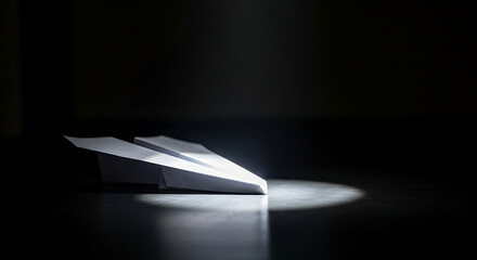Paper airplane on a dark surface illuminated by a single spotlight beam