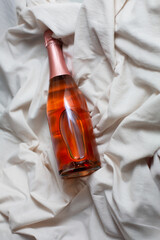 champagne sparkling wine bottle mockup with elegant rose-colored liquid resting on soft white fabric, showcasing luxurious design and inviting ambiance for creative projects