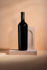 Red wine bottle mockup displayed on a minimalist stone base against a soft peach background, showcasing elegant design and modern aesthetics for branding and marketing purposes