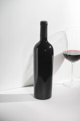 Wine bottle mockup with elegant design, showcasing glossy finish and shadows, accompanied by a glass of red wine, perfect for branding and marketing concepts