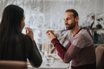 Two individuals share a relaxed meal while having a conversation in a casual dining space. The atmosphere appears cheerful and friendly, capturing the joy of socializing over delicious food.