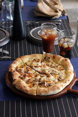 Freshly baked mushroom cheese pizza on wooden tray served with iced coffee and cola in glasses on dining table.