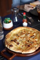 Freshly baked mushroom cheese pizza on wooden tray served with iced coffee and cola in glasses on dining table.