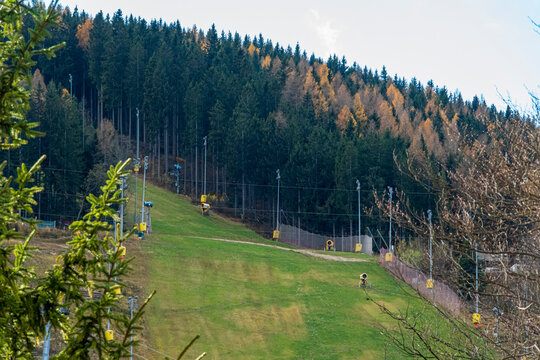 Ski slope with snow cannons on green hillside in autumn mountain forest, Austria.