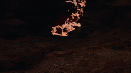 Glimmers of orange light emerge from within a dark cave, casting shadows on rocky surfaces. The ambiance hints at mystery, creating a captivating contrast with the twilight surroundings.